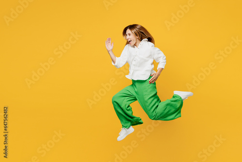 Full body side profile view young excited caucasian happy woman she wears white shirt casual clothes jump high run fast hurry up isolated on plain yellow background studio portrait. Lifestyle concept. © ViDi Studio