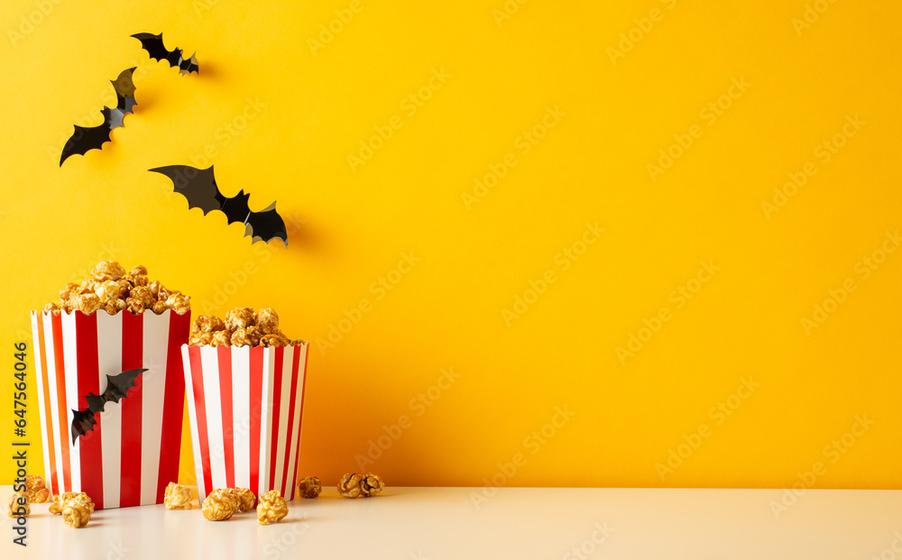 Halloween cinema adventure with buddies. Side view image of table and wall dressed with spooky bats. Popcorn boxes await. Perfect for ads on a yellow wall Halloween cinema adventure with buddies. Side view image of table and wall dressed with spooky bats. Popcorn boxes await. Perfect for ads on a yellow wall