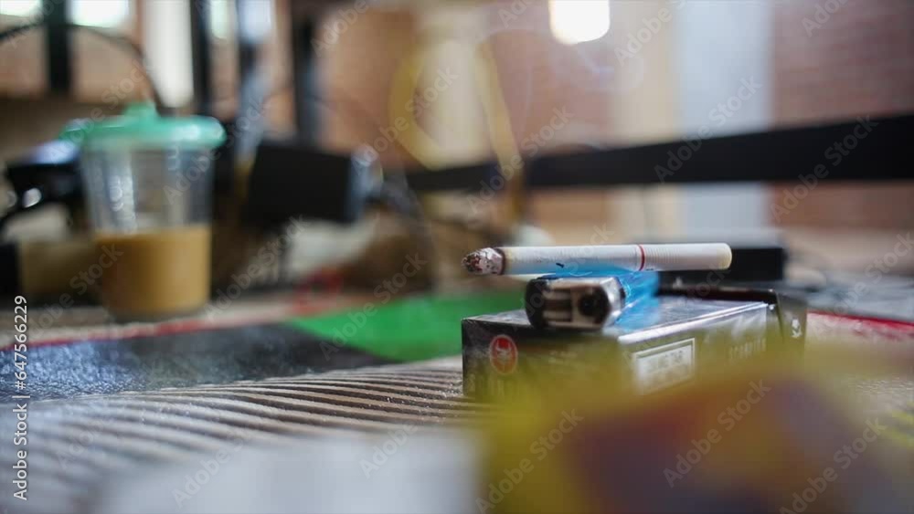 Closeup of cigarette on cigarette packs and gas lighters with beautiful wisps of smoke with a background of a glass of coffee with milk and cables scattered in the workers' room Closeup of cigarette on cigarette packs and gas lighters with beautiful wisps of smoke with a background of a glass of coffee with milk and cables scattered in the workers' room