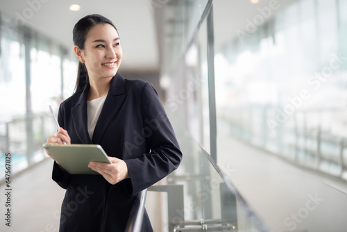 Asian business woman holding a tablet looking away, Fashion business photo of beautiful girl in casual suite with tablet .