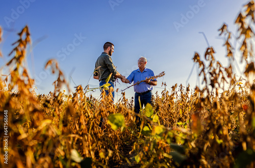 Two farmers in soy field making agreement with handshake before harvest at sunset.