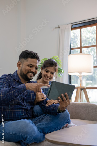 Happy Young couple using a digital tablet together while relaxing on couch sofa at home