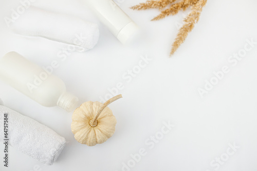 Plastic container for shampoo without etiket and pumpkin with towels on a white background. Cosmetics bottle mockup with autumn leaves.