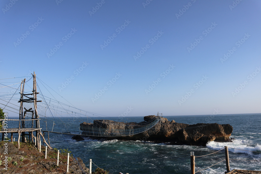 a bridge over the sea connecting shore and rocky cliff 