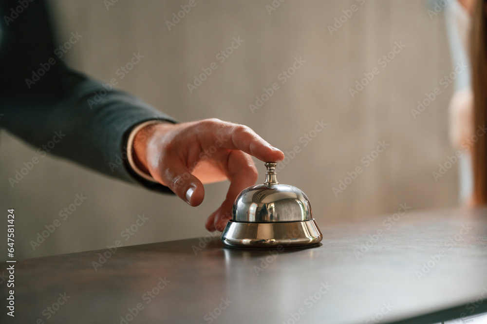 Close up view, using hotel desk bell. A man in a black jacket at the hotel reception Close up view, using hotel desk bell. A man in a black jacket at the hotel reception
