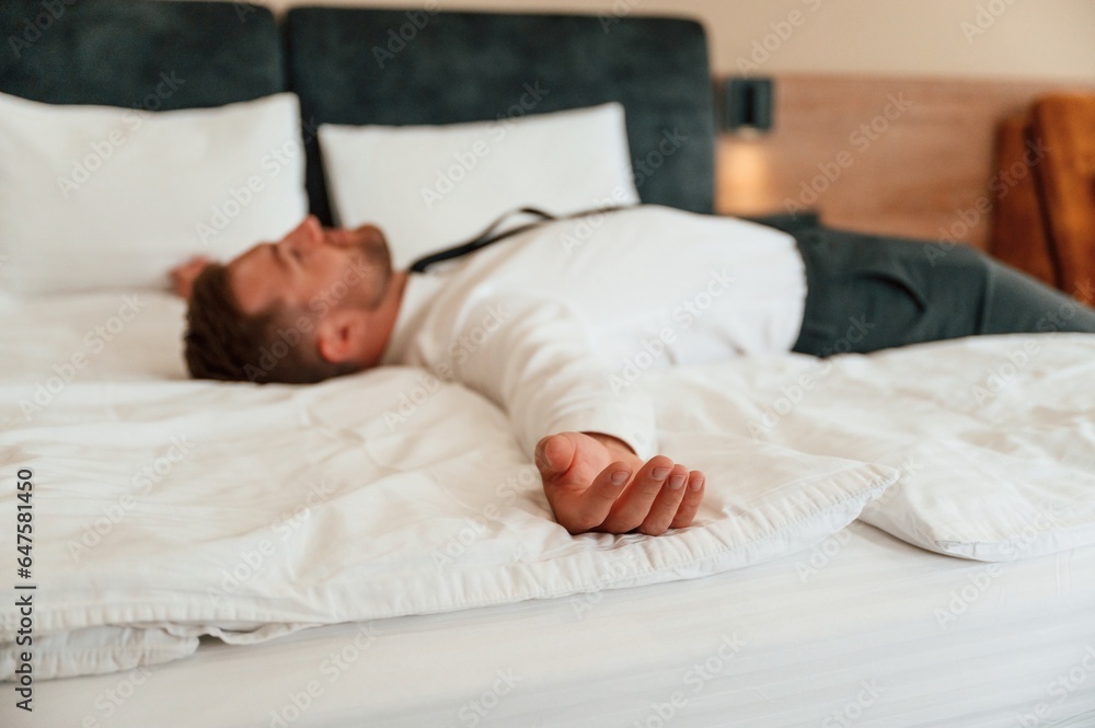Tired, lying down on the bed. Businessman is indoors in the hotel room Tired, lying down on the bed. Businessman is indoors in the hotel room