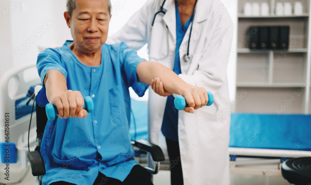 Asian physiotherapist helping elderly man patient stretching arm during exercise correct with dumbbell in hand during training hand in bed in clinic Asian physiotherapist helping elderly man patient stretching arm during exercise correct with dumbbell in hand during training hand in bed in clinic
