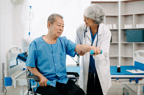 Asian physiotherapist helping elderly man patient stretching arm during exercise correct with dumbbell in hand during training hand in bed in clinic