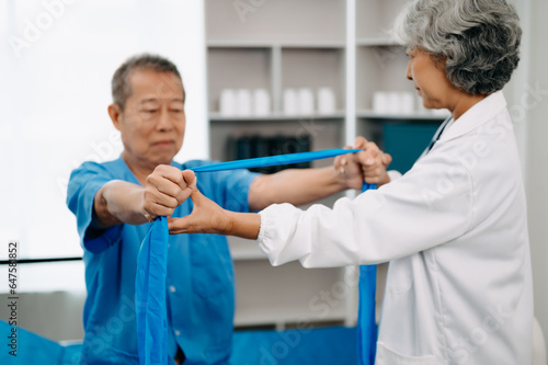 Asian physiotherapist helping elderly man patient stretching arm during exercise correct with dumbbell in hand during training hand in bed in clinic