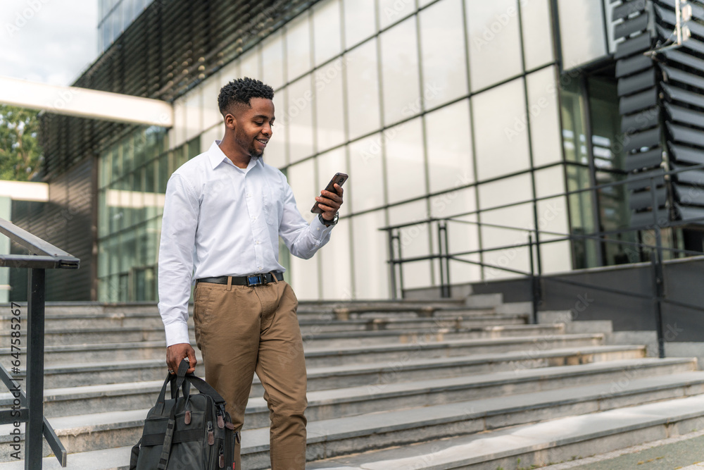 With purpose in his stride, the stylish African-American businessman carries his laptop bag and holds his phone, ready to conquer the day's challenges. With purpose in his stride, the stylish African-American businessman carries his laptop bag and holds his phone, ready to conquer the day's challenges.