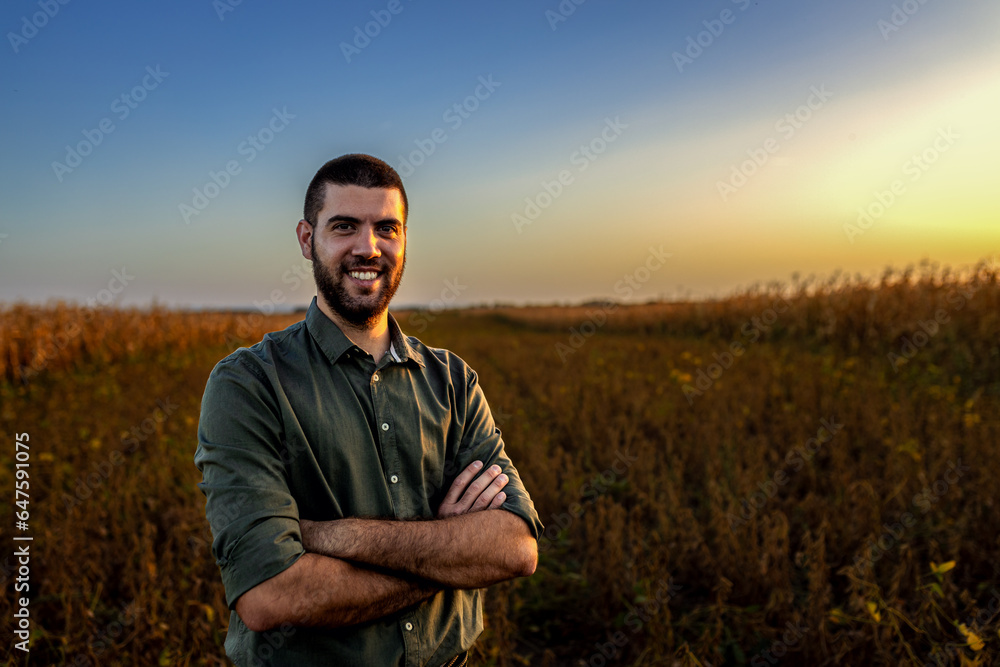 Portrait of young farmer standing in a soy field at sunset looking at camera. Portrait of young farmer standing in a soy field at sunset looking at camera.