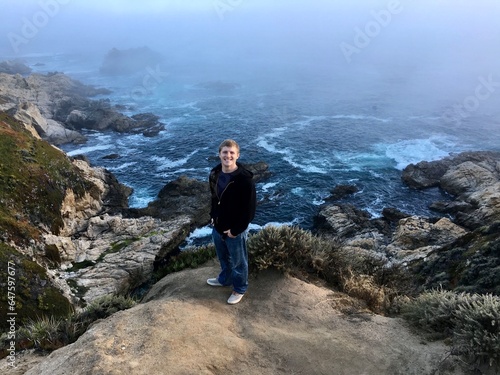 Smiling young man standing on coastal rocks off Highway 1, Carmel-by-the-sea, Monterey Peninsula, California, USA photo