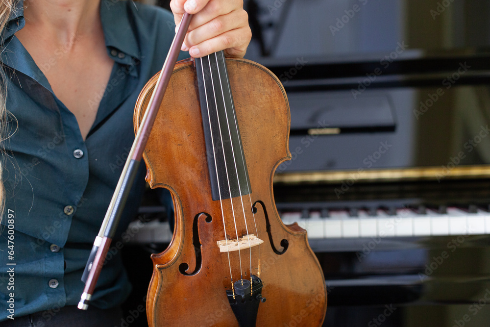 Frau hält Geige in Hand mit Klavier im Hintergrund.
Woman holding violin in hand with piano in background. Frau hält Geige in Hand mit Klavier im Hintergrund.
Woman holding violin in hand with piano in background.