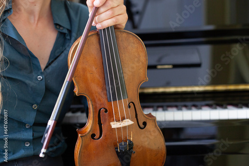Frau hält Geige in Hand mit Klavier im Hintergrund. Woman holding violin in hand with piano in background.