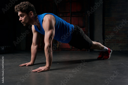 full length of strong man in sportswear training in plank pose in darkness of night street