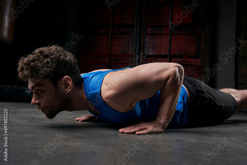 relentless man in blue tank top doing push-ups while working out on city street at night