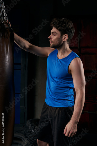 sportive man in blue tank top standing near punching bag on city street at night