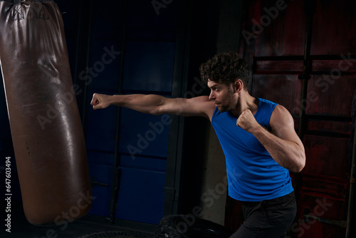 unshaven sportive man boxing punching bag in darkness on urban street, outdoor workout