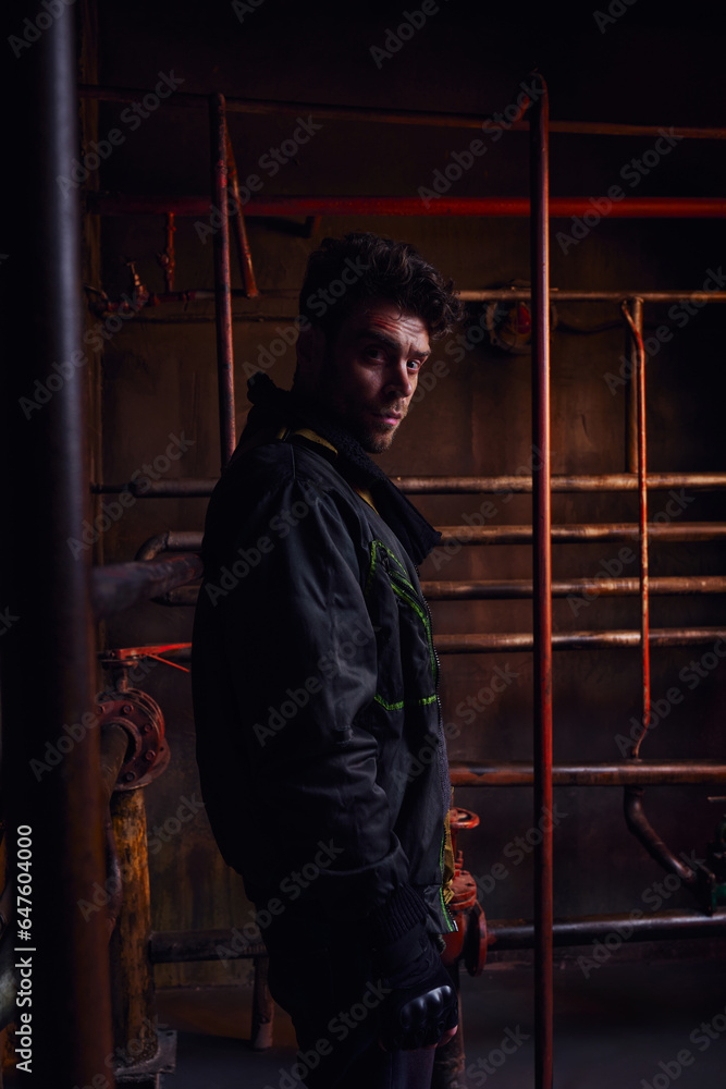 despaired unshaven man looking at camera next to rusty pipelines in abandoned post-disaster subway despaired unshaven man looking at camera next to rusty pipelines in abandoned post-disaster subway