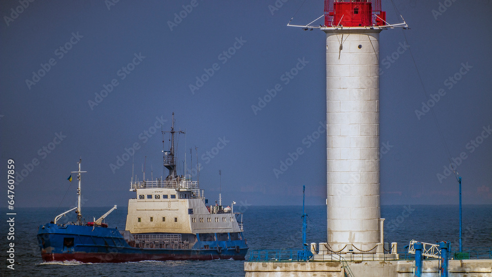 A white and blue ship sails past the red and white Odessa lighthouse