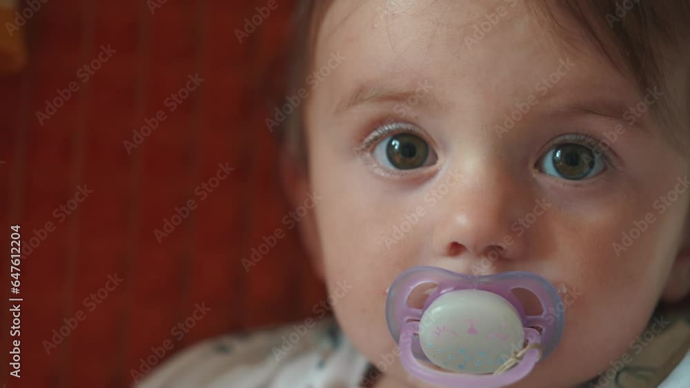 a small newborn sits on the couch with a pacifier in his mouth. happy family childhood dream concept. a little child with a purple pacifier sits and looks at the camera close-up lifestyle a small newborn sits on the couch with a pacifier in his mouth. happy family childhood dream concept. a little child with a purple pacifier sits and looks at the camera close-up lifestyle