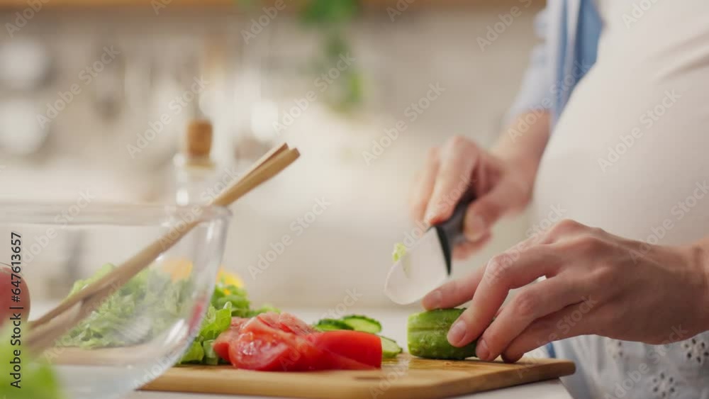 Tummy. Housewife parent cutting fresh cucumbers in housewife's home kitchen. The expectant mother uses a knife to cut slices for snacks and masters new combinations of vegetables and ingredients. Tummy. Housewife parent cutting fresh cucumbers in housewife's home kitchen. The expectant mother uses a knife to cut slices for snacks and masters new combinations of vegetables and ingredients.