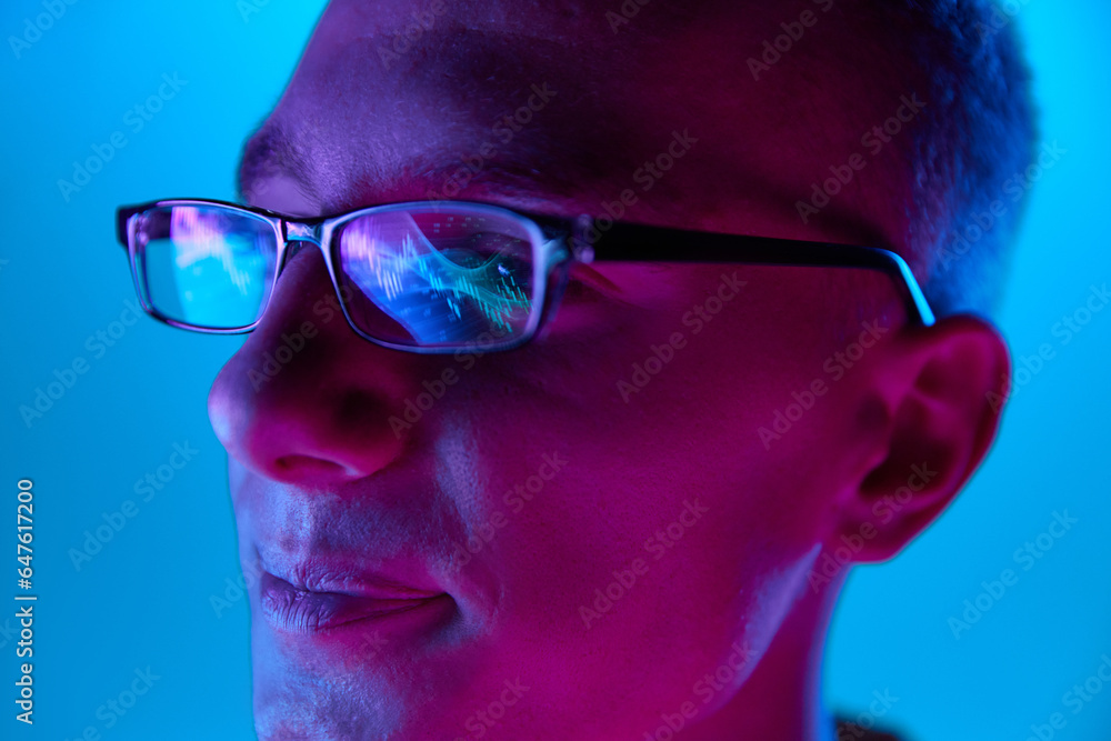 Close Up side view portrait of young handsome guy, student in glasses reflects scoring, rates, graphs isolated on blue background in red neon light, filter. Close Up side view portrait of young handsome guy, student in glasses reflects scoring, rates, graphs isolated on blue background in red neon light, filter.