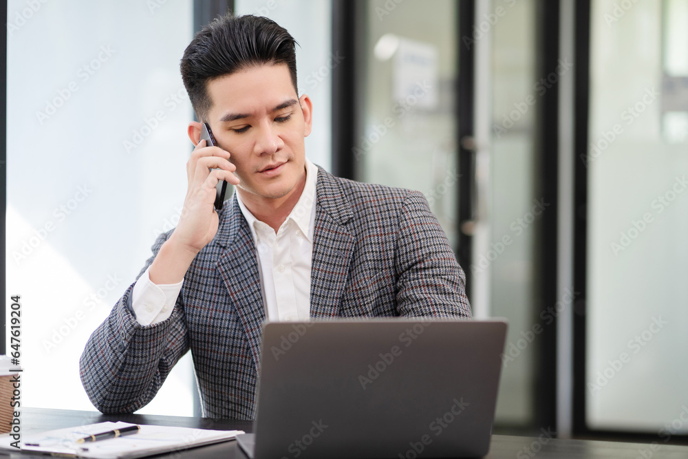 Smiling Asian young freelancer working from home remotely.He is talking on the phone. Smiling Asian young freelancer working from home remotely.He is talking on the phone.