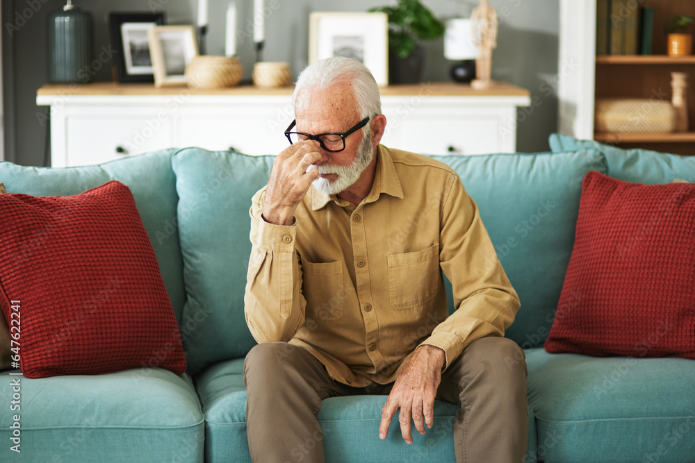 A senior man suffering from a migraine while sitting on the sofa in the living room
