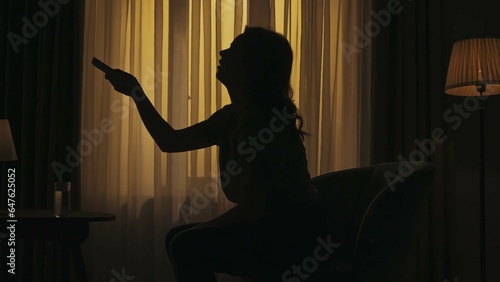 Everyday life creative concept. Woman sitting on a chair holding glass of water, switching on air conditioner.