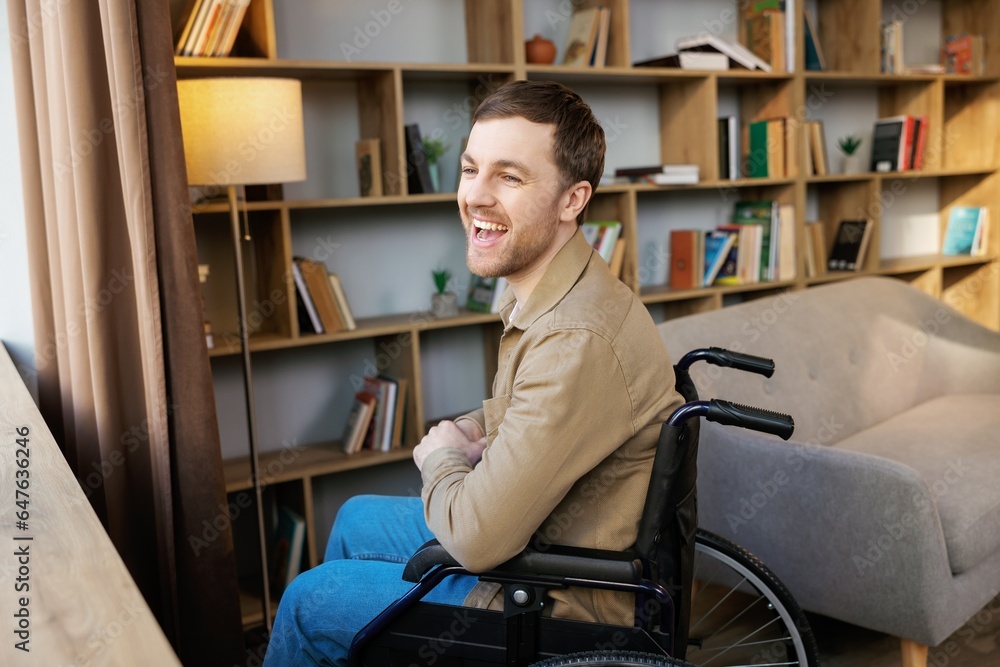 Man on wheelchair in room looking through window and smiling. Side view of young disabled patient in wheelchair looking out window Man on wheelchair in room looking through window and smiling. Side view of young disabled patient in wheelchair looking out window