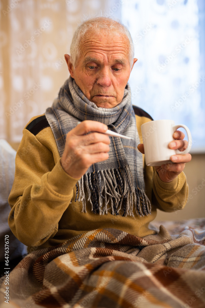 Old man wrapped in blanket measuring body temperature Old man wrapped in blanket measuring body temperature