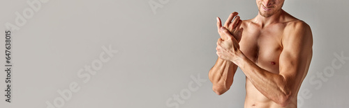 Hand pain, sprain. Cropped image of muscular man with relief body in underwear holding wrist against grey background. Concept of men's health and beauty, body care, fitness. Banner. Copy space for ad