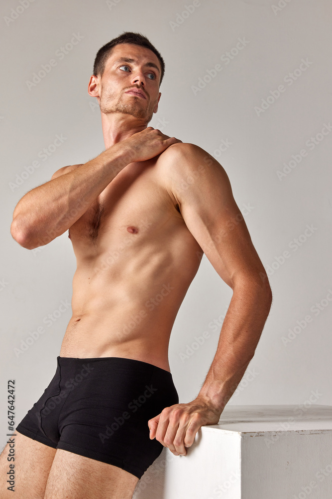 Fototapeta premium Portrait of handsome man with muscular, athletic body shape posing shirtless in underwear against grey studio background. Concept of men's health and beauty, body care, fitness, wellness, ad