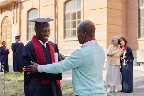 Dad congratulating his son with graduation from university while standing outdoors