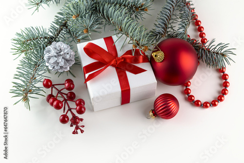 A white box with a gift tied with a red ribbon, a spruce branch and obligatory decorations on a white background