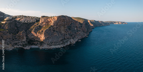 Aerial view of Breathtaking coastal panorama with clear blue sea, rugged cliffs, and the serene tranquility of small holiday houses, Cala Moraig, Zona Encinas, Cumbre del Sol, Alicante, Spain. photo