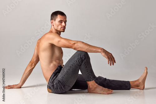 Man with muscular, strong, relief body, posing shirtless in jeans against grey studio background. Confidence. Concept of men's health and beauty, fashion, body care, fitness, wellness, ad
