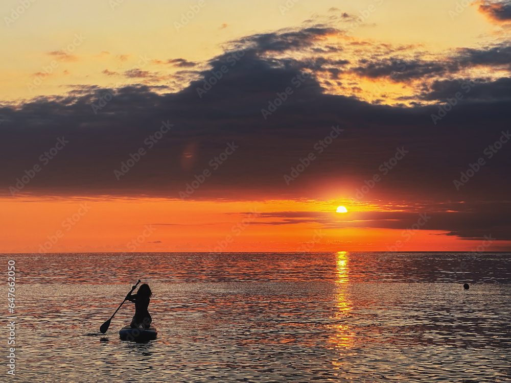 Silhouette of woman on Sub Board on sea surface at sunset. Stand up paddle boarding concept.