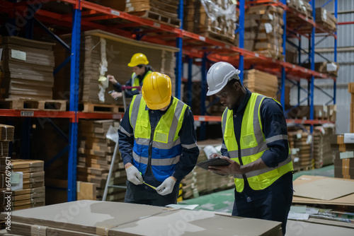 An employee checks products in a warehouse with a tablet. They are working together in the factory.