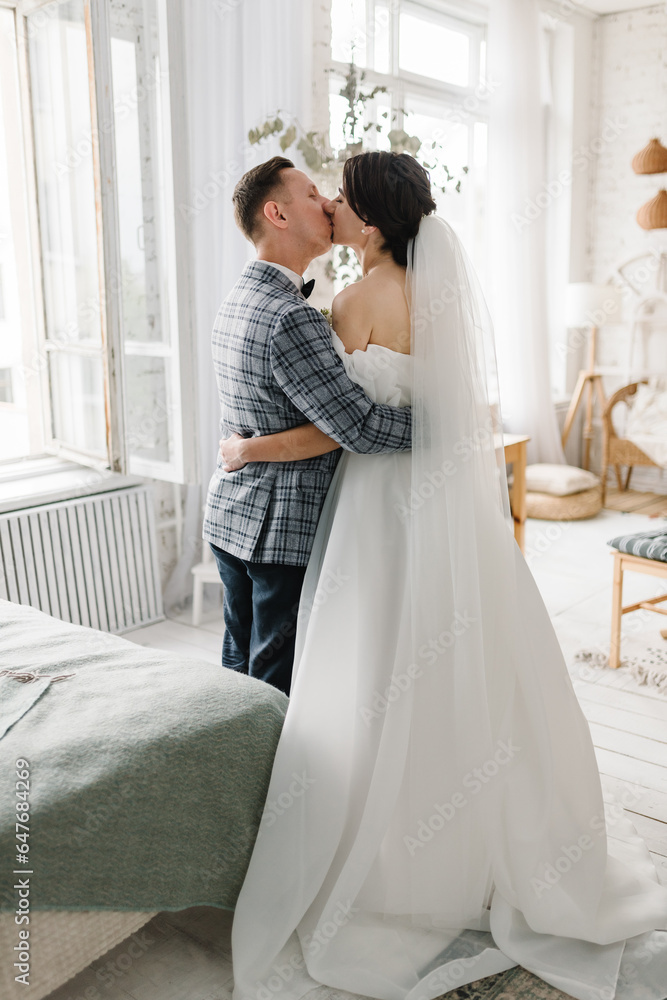 First meeting is newlyweds in interior in bedroom. Couple in love. Bride kisses groom at home. Handsome man and woman posing together. Happy wedding day of marriage. Photo session at studio. Back view First meeting is newlyweds in interior in bedroom. Couple in love. Bride kisses groom at home. Handsome man and woman posing together. Happy wedding day of marriage. Photo session at studio. Back view