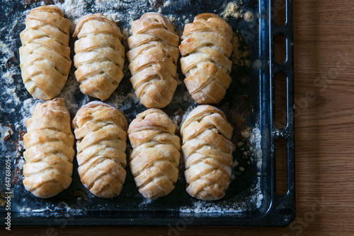 Traditional russian pies pirozhki on baking pan on brown table, top view, selective focus.