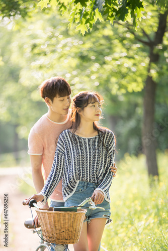 A young male and female couple are enjoying a walk on a bicycle in the park.