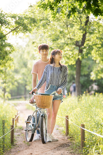 A young male and female couple are enjoying a walk on a bicycle in the park.