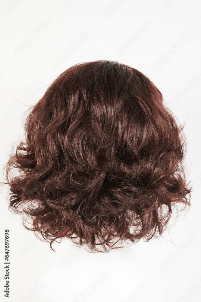 Naklejka premium Natural looking dark brunet wig on white mannequin head. Middle length brown hair on the plastic wig holder isolated on white background, back view.