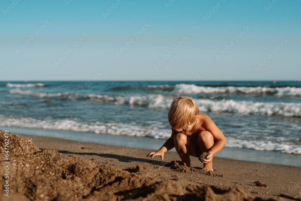 little boy 3 years old plays in the sand on the beach near the sea