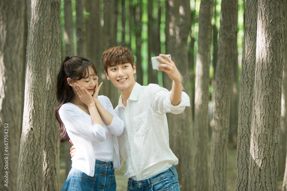 A lovely young couple are having a great time taking pictures using their smartphones in a forested park. A lovely young couple are having a great time taking pictures using their smartphones in a forested park.
