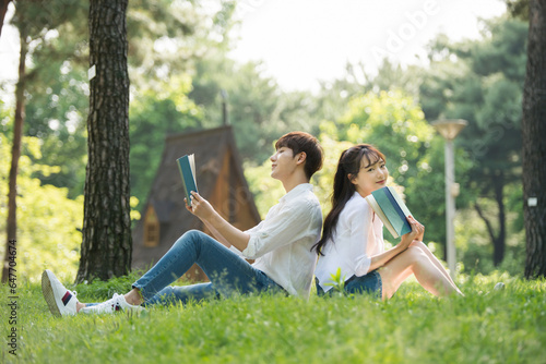 A young male and female couple are enjoying a pleasant picnic while drinking drinks and reading books on the forested park lawn.