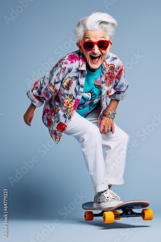 Funny and happy old woman uses a skateboard and enjoys doing stunts - isolated on light blue background