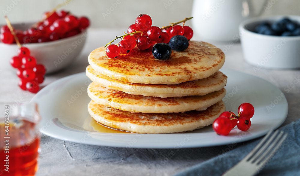Pile of pancakes with red currants, blueberries and honey on a grey plate with fork Pile of pancakes with red currants, blueberries and honey on a grey plate with fork